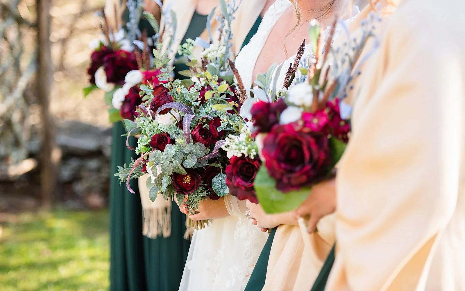 Closeup of bridesmaid bouquets with burgundy flowers and greenery, bridesmaids wearing dark green dresses.