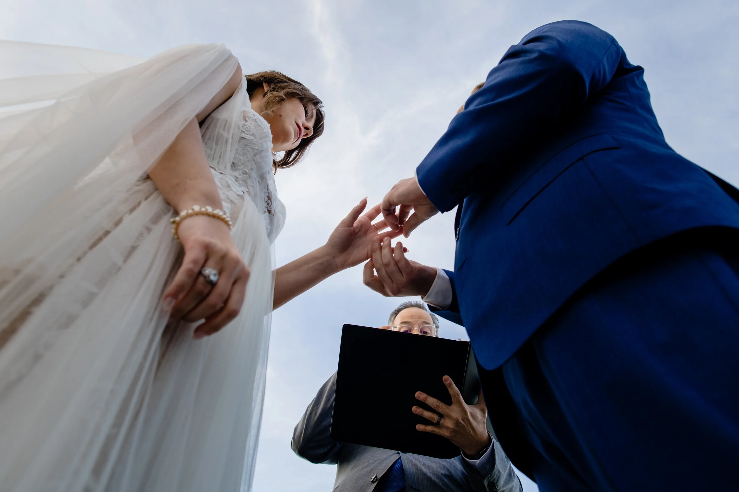 Low angle view of the couple exchanging rings during an outdoor wedding ceremony with the officiant in the background.