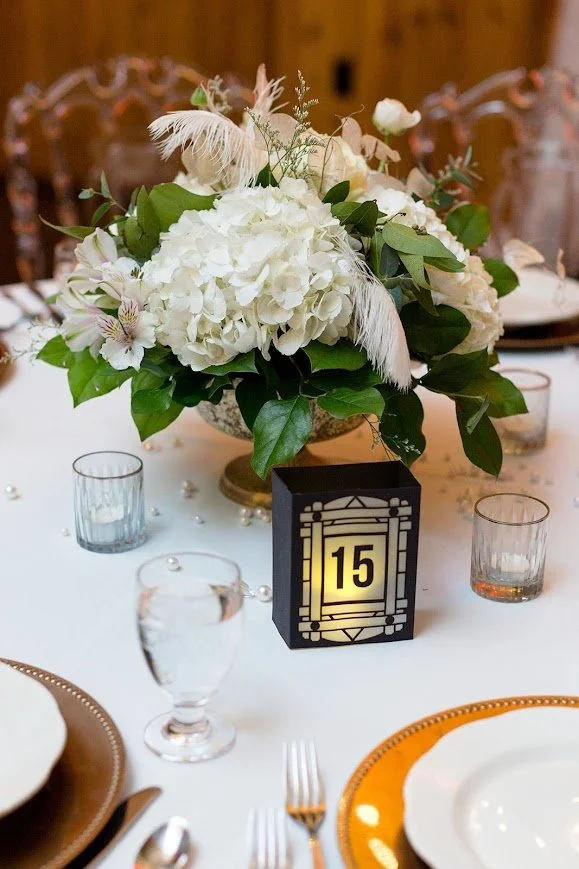 White floral centerpiece with table number 15 on an elegantly set wedding reception table