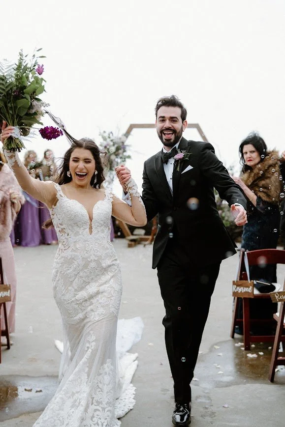 Bride and groom walk back down the aisle smiling as guests celebrate around them at the wedding exit.