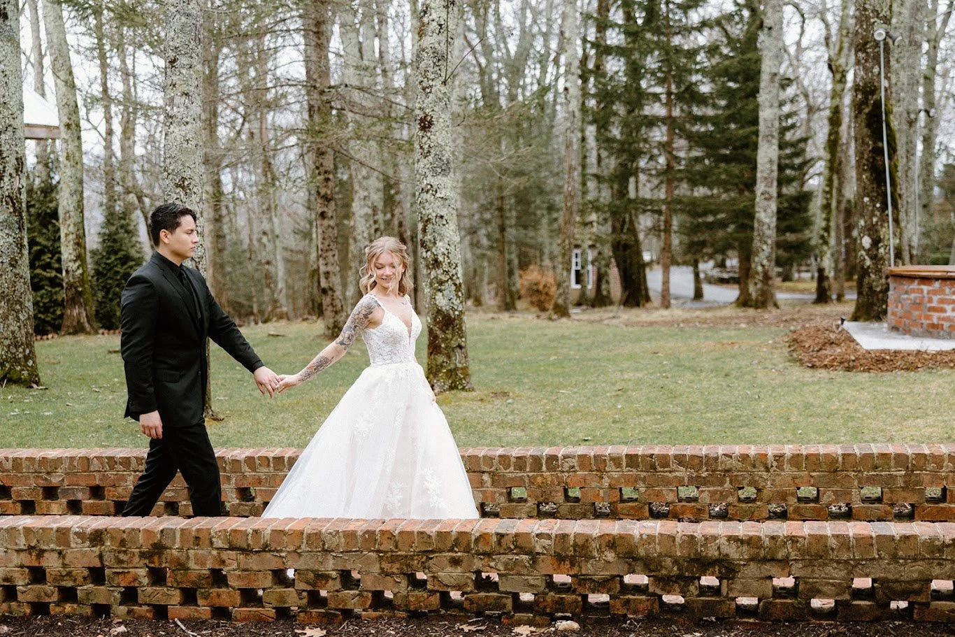Bride and groom walking hand in hand along a brick garden wall on the wedding day