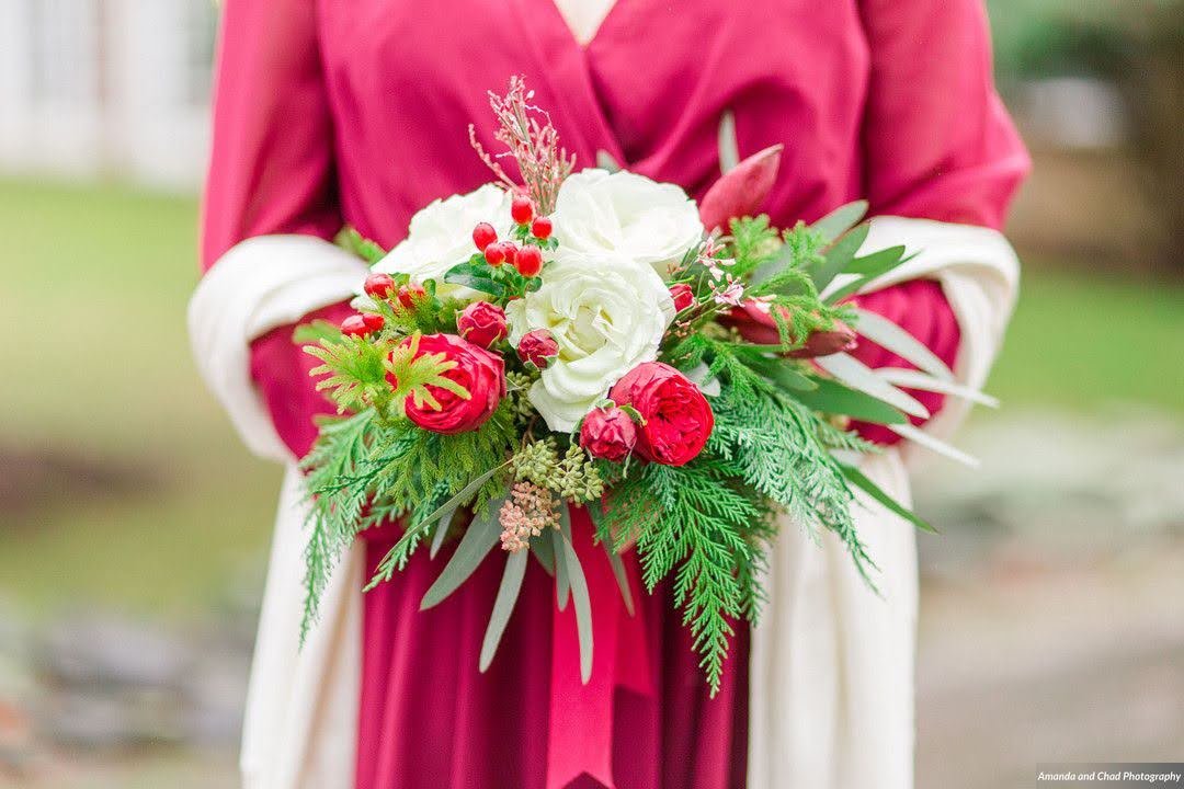 Closeup of a bridesmaid bouquet with red and white flowers and evergreen greenery.