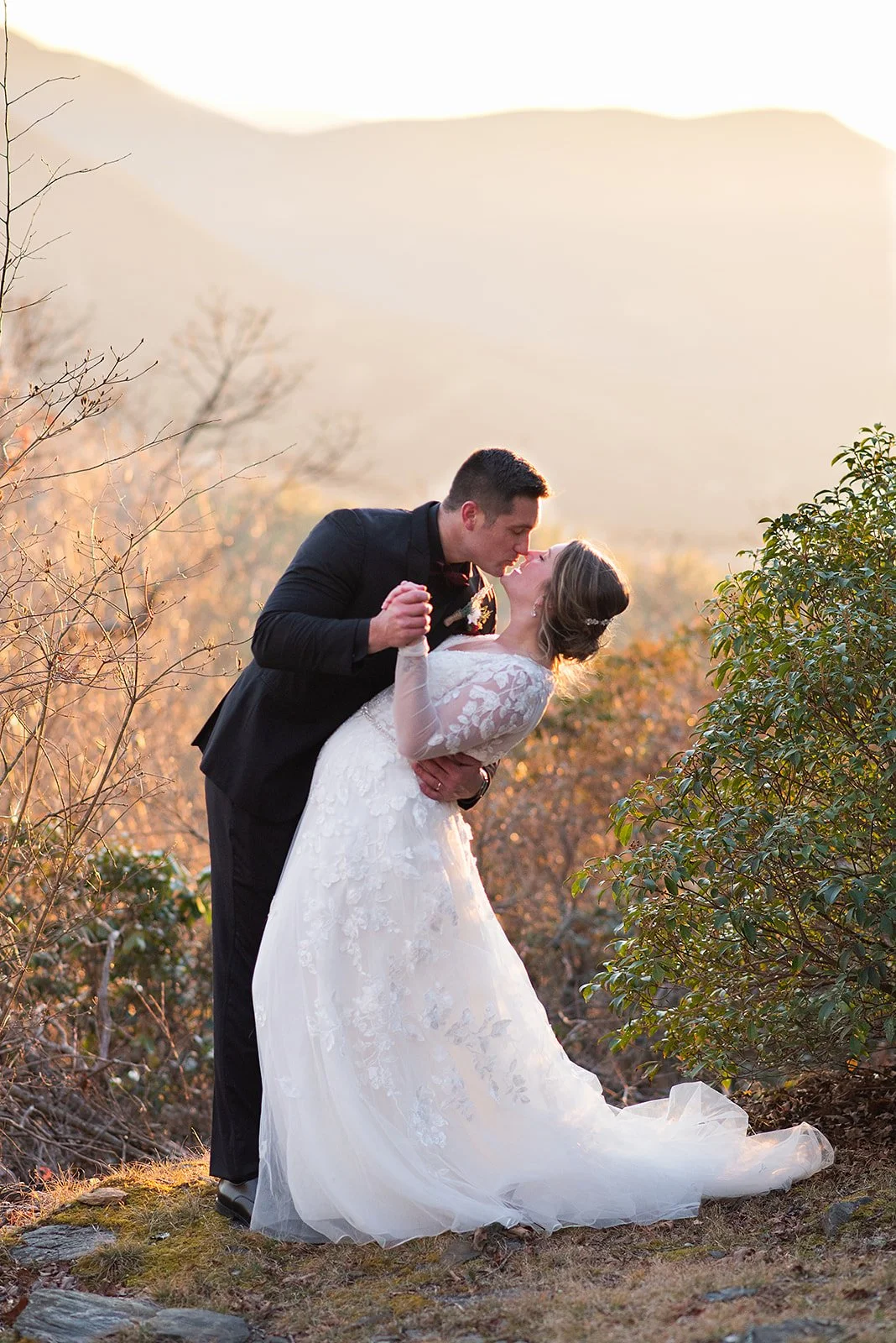Bride and groom sharing a dip kiss at sunset with a mountain view in the background