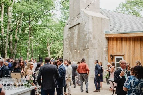 Wedding guests mingle and socialize outdoors near a building with string lights.