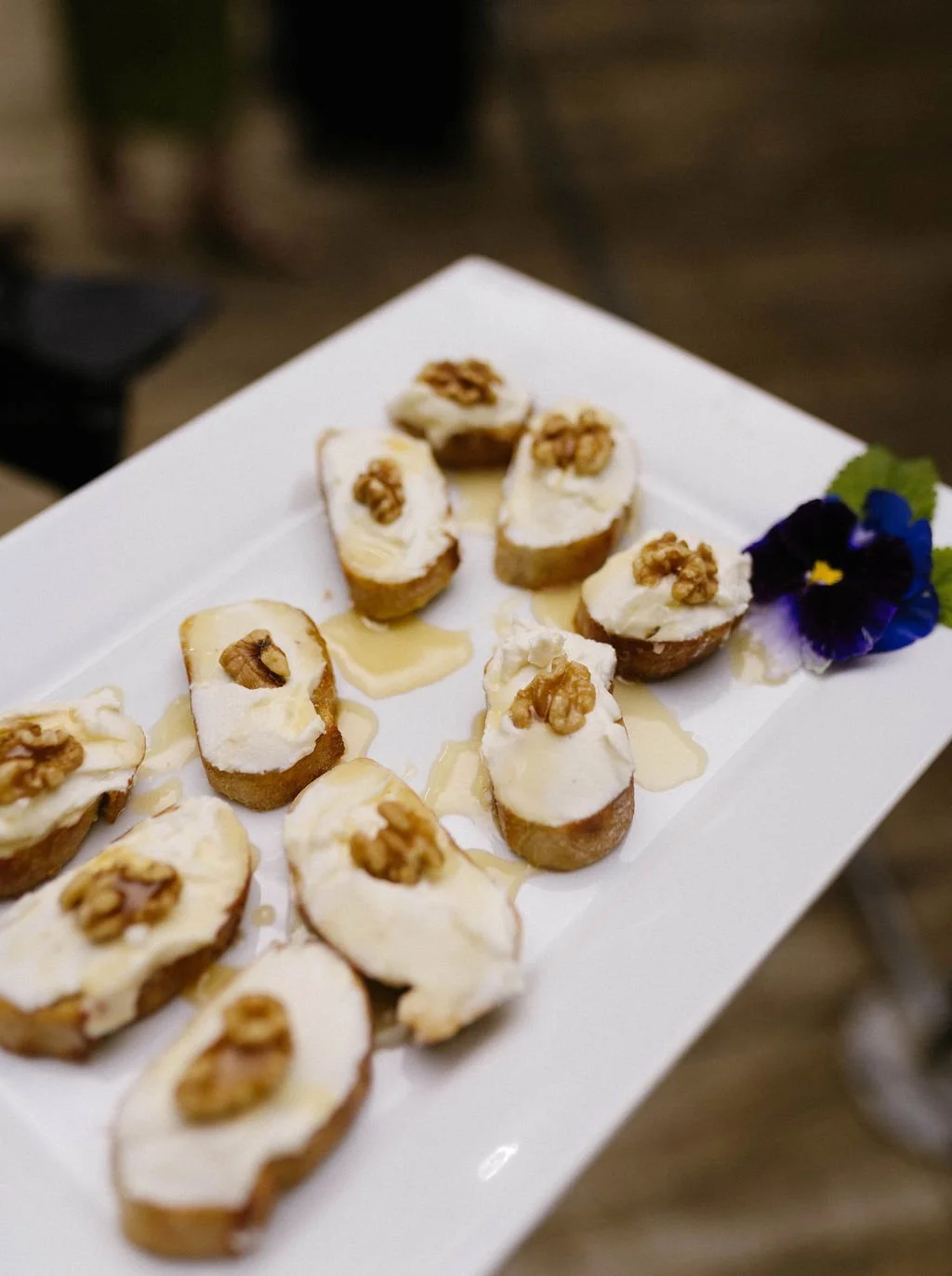 Goat cheese crostini topped with walnuts and drizzled honey on a white platter