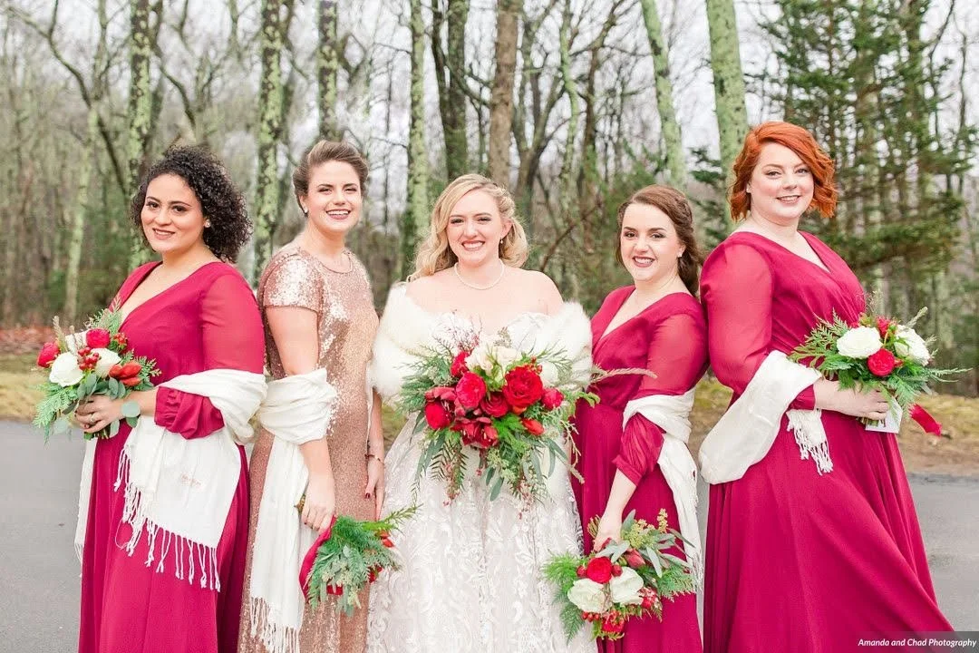 Bridal party winter portrait with bridesmaids in magenta dresses and white wraps standing outdoors.