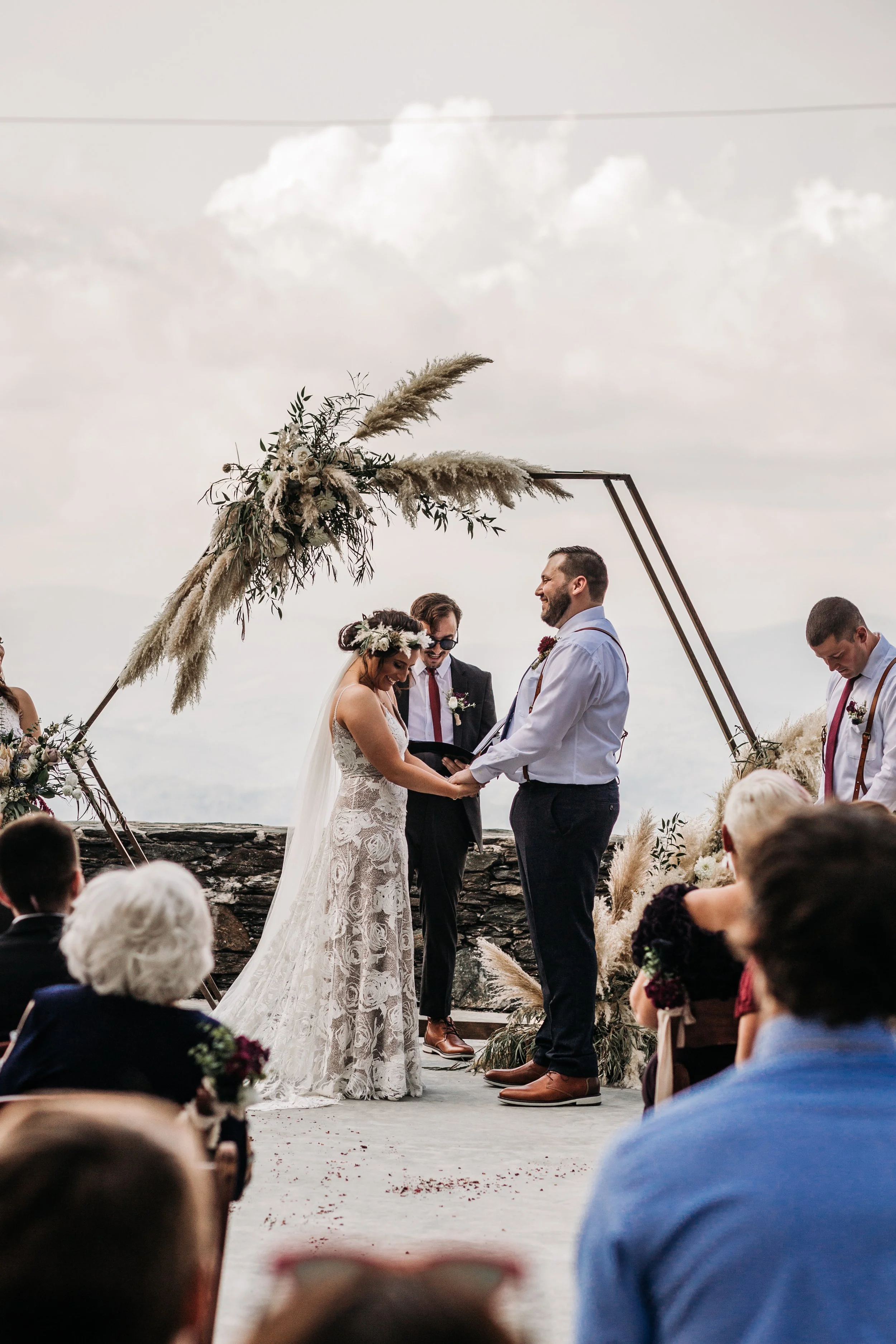 Bride and groom holding hands during vows beneath a geometric arch at an outdoor mountain ceremony.