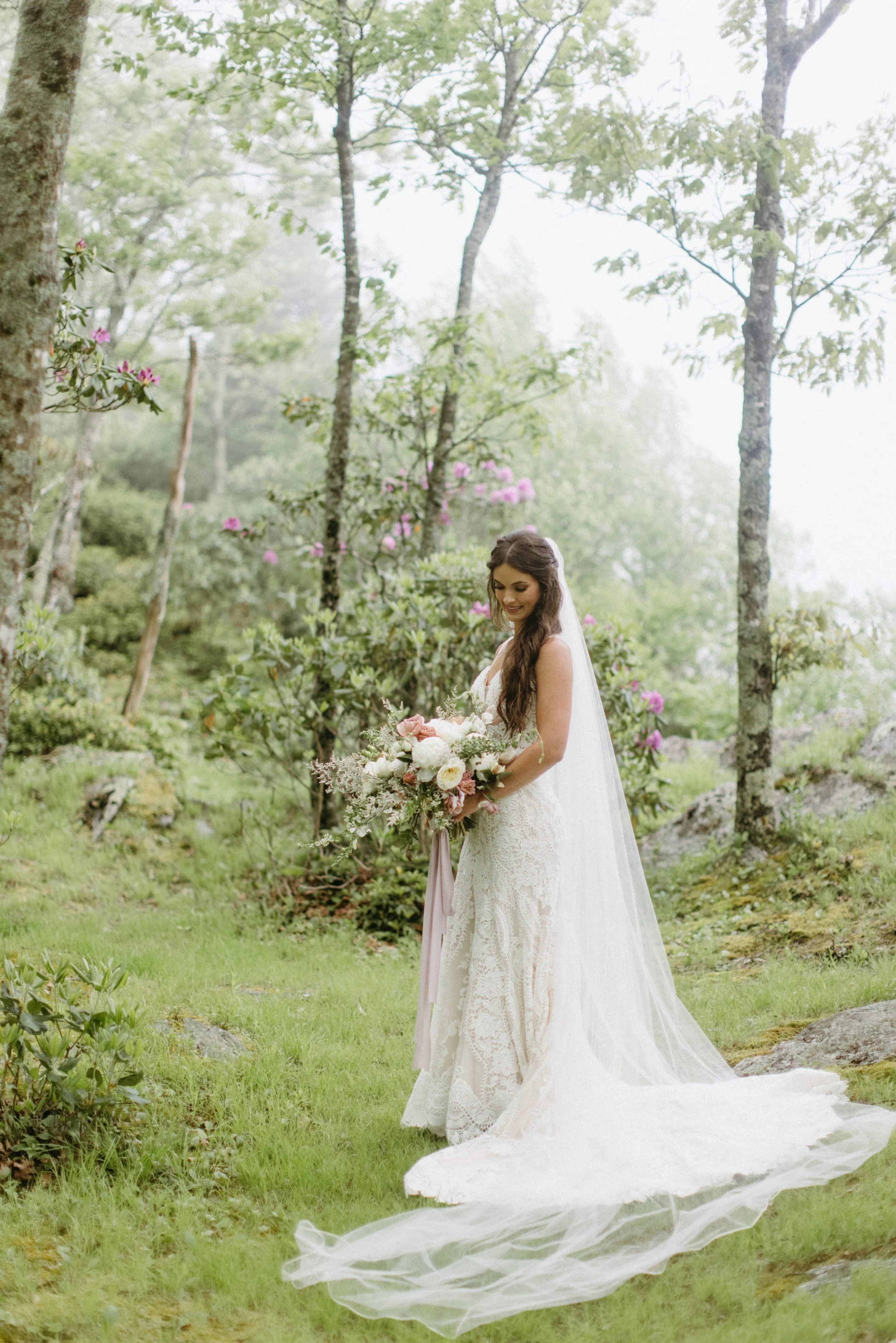 Bride holding a bouquet in a misty forest with a long veil and train flowing behind