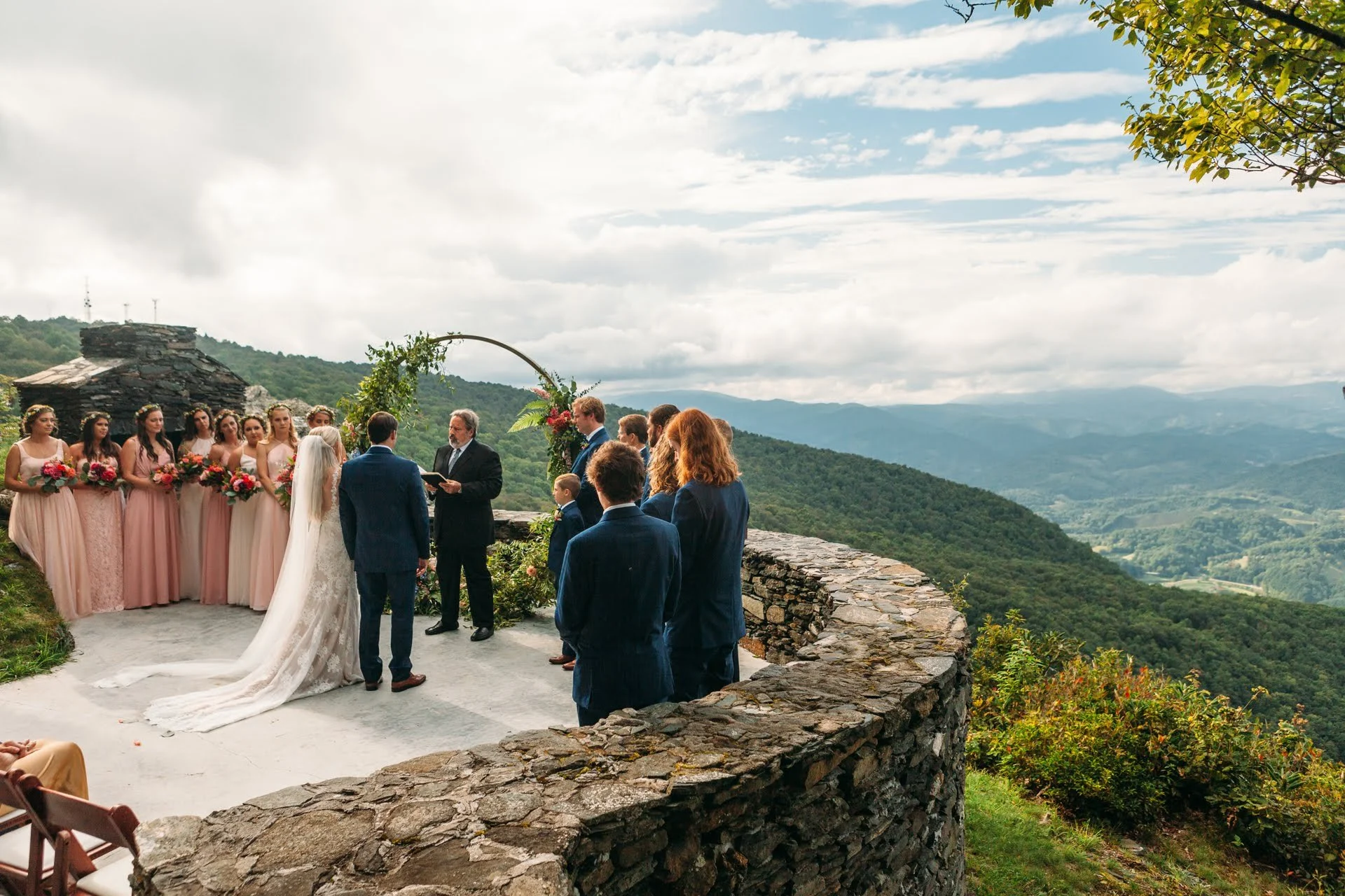 Wedding ceremony at a mountain overlook with an arch, wedding party, and panoramic views.