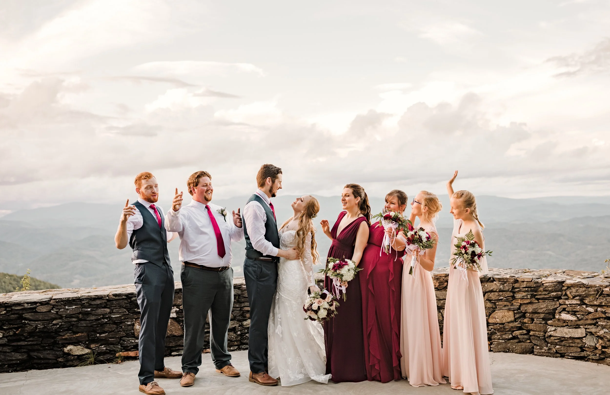 Fun wedding party photo at a mountain overlook with the bride and groom in the center.
