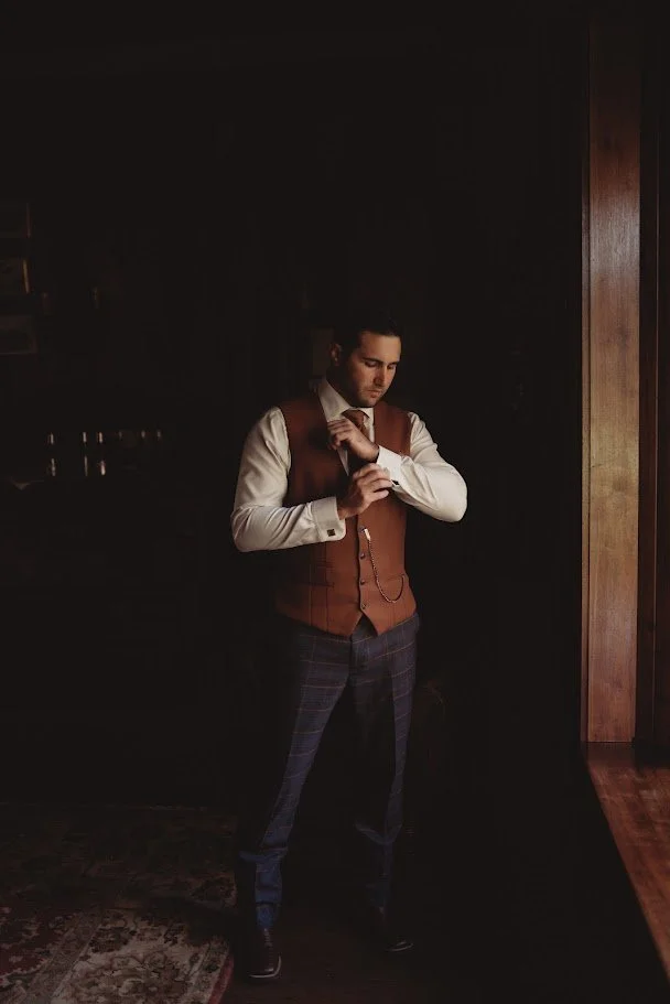 Groom adjusting his cufflinks while getting ready in a dimly lit room