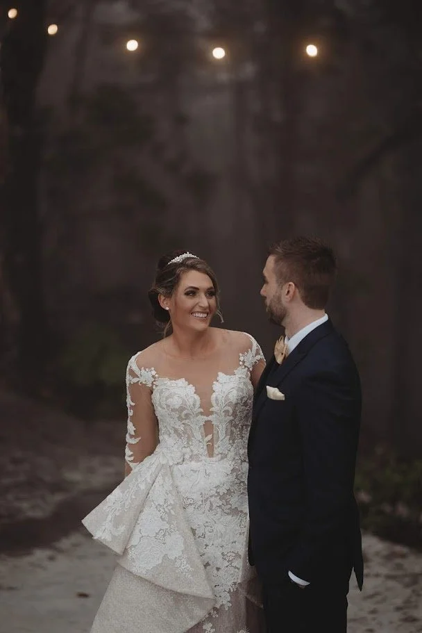 Bride smiling at the groom during a foggy forest portrait, wearing a lace wedding dress.