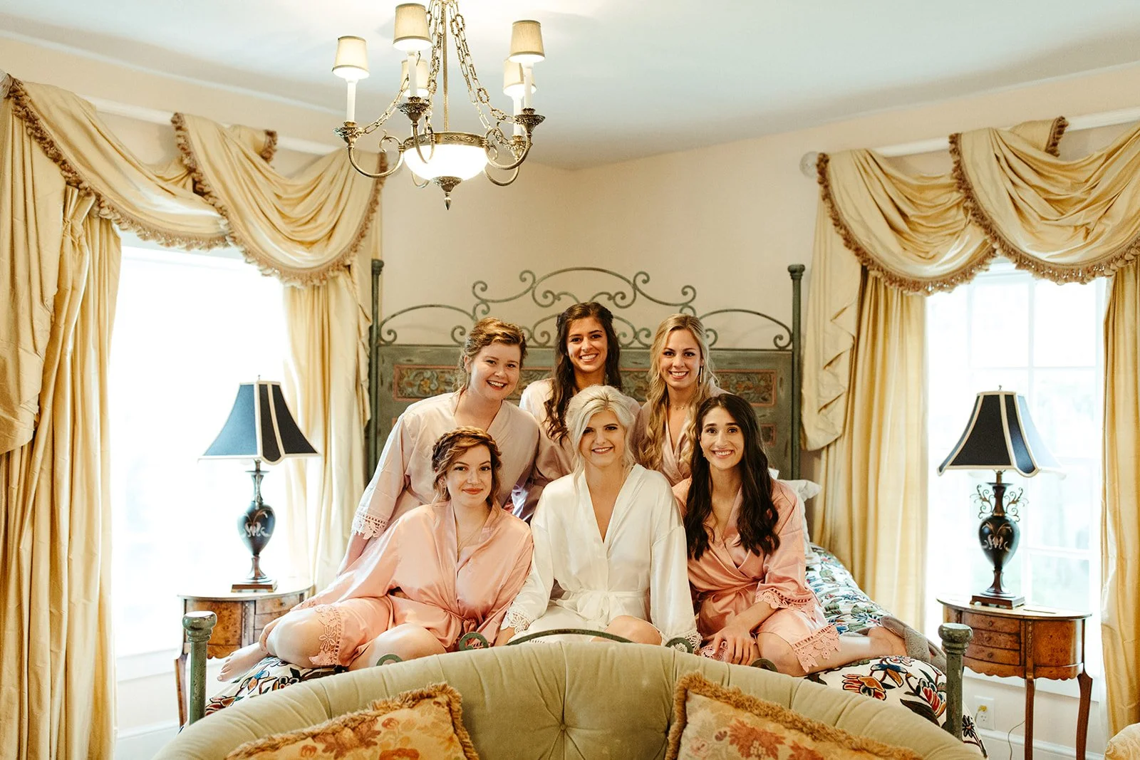 Bride and bridesmaids smiling together in satin robes while getting ready before the wedding.