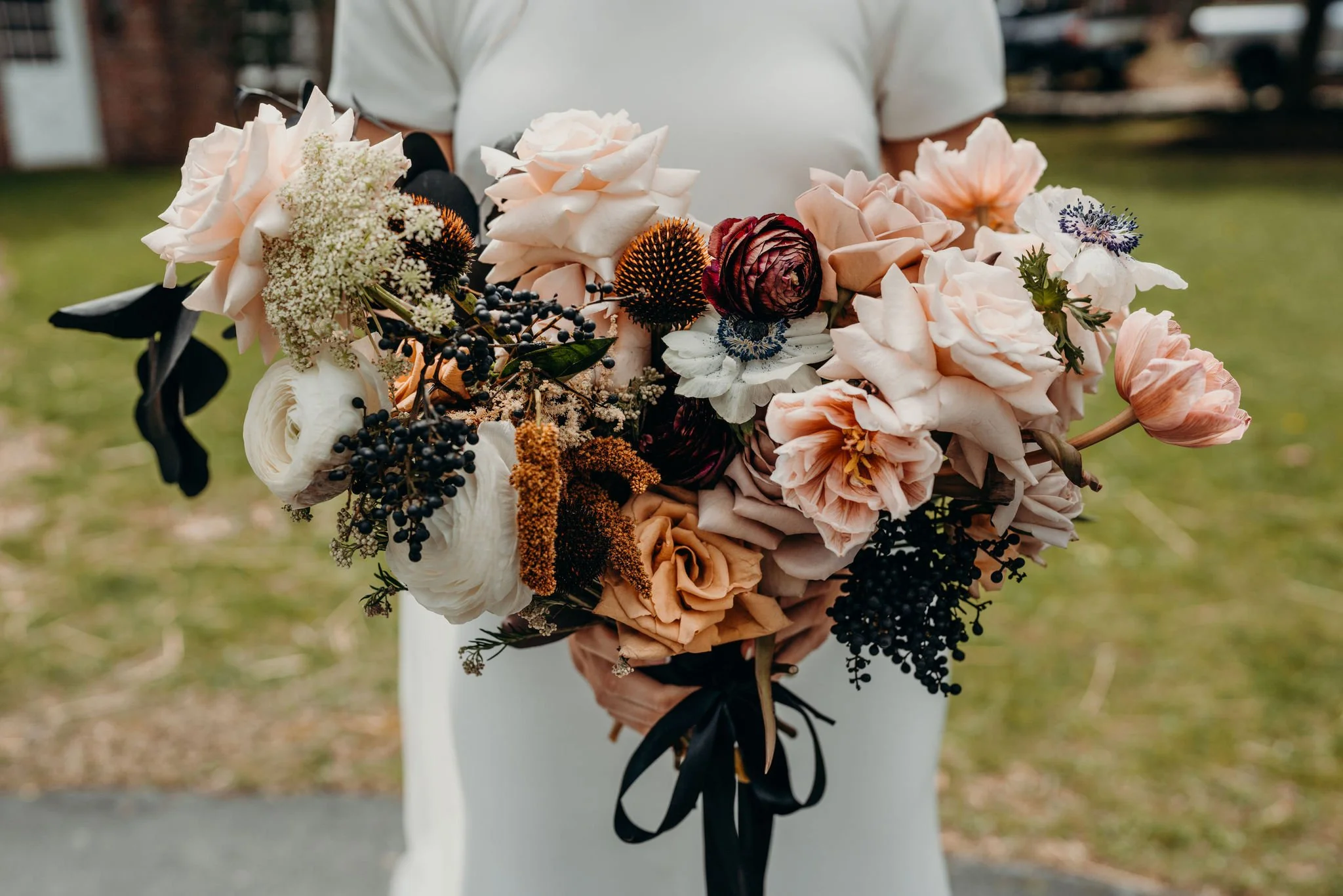 Closeup of a bridal bouquet with blush roses, burgundy flowers, and a black ribbon wrap.