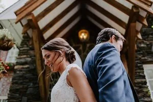 Bride and groom standing back to back for a first look near a wooden ceremony entrance