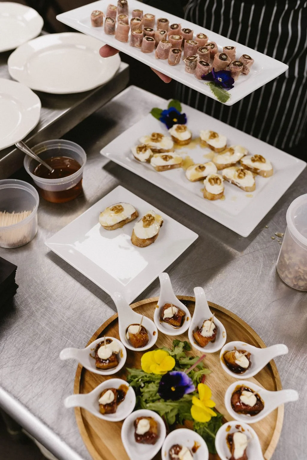 Assorted wedding cocktail hour canapes arranged on white serving plates with edible flowers and sauces.
