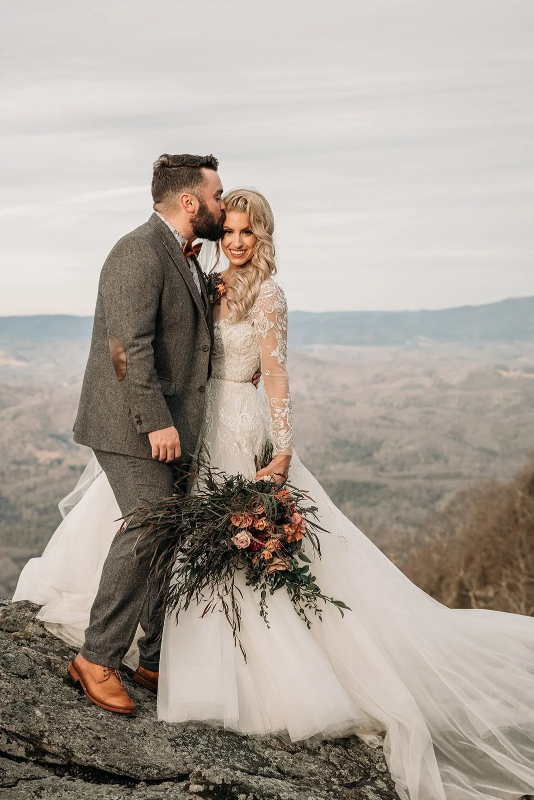 Close portrait of bride and groom on a mountain overlook with the bride holding a moody bouquet.