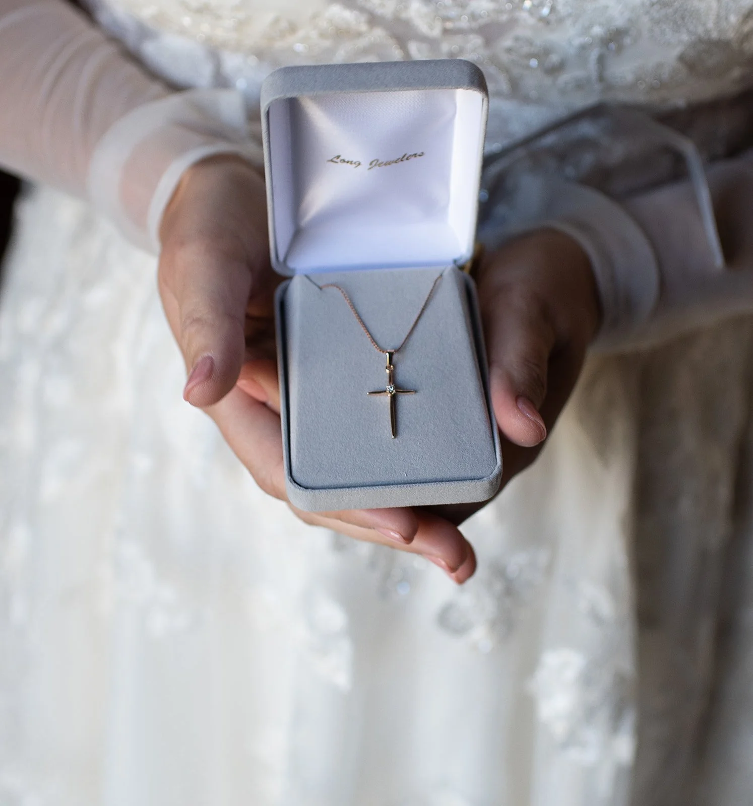 Cross necklace presented in a jewelry box held in hands for a wedding detail photo.