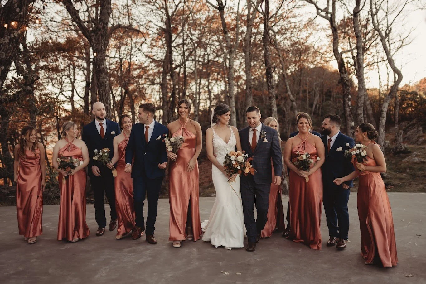 Wedding party walking together in a line with fall trees in the background