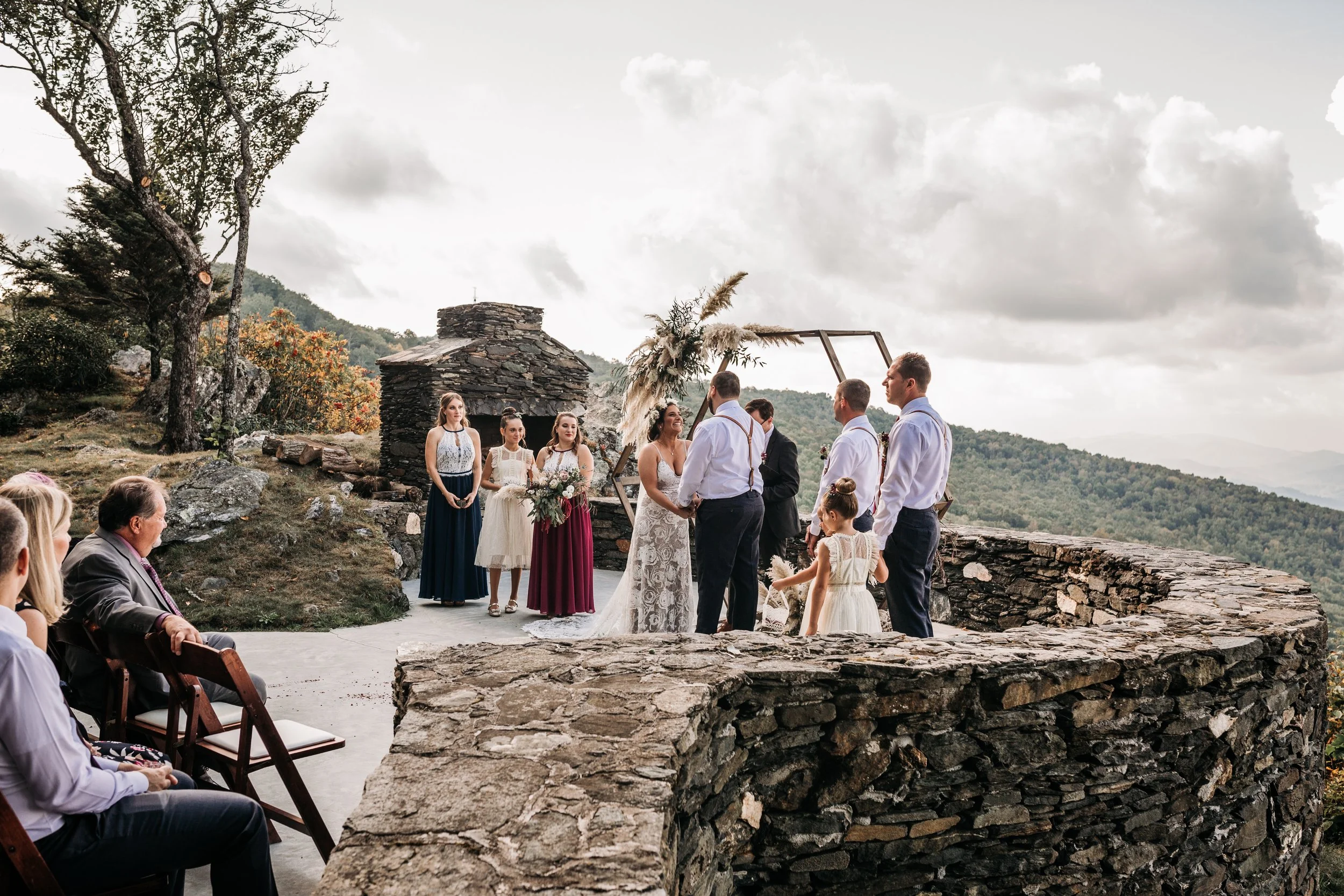 Guests watching a wedding ceremony on a stone terrace with mountain views in the background.