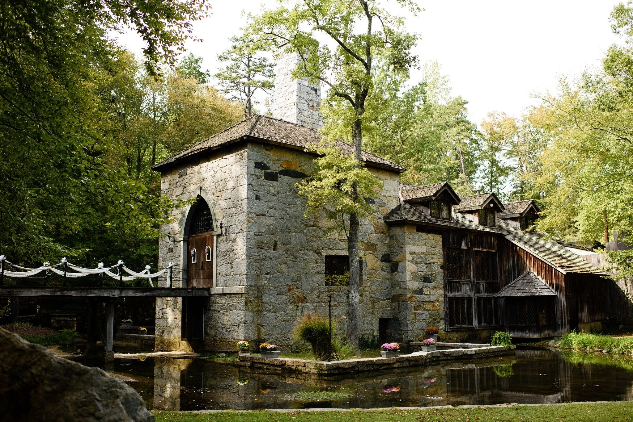 Stone mill wedding venue beside a pond with a small bridge and trees surrounding the building