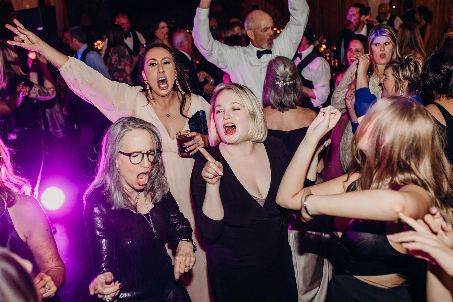 Wedding reception dance floor with purple lighting and guests singing and dancing.