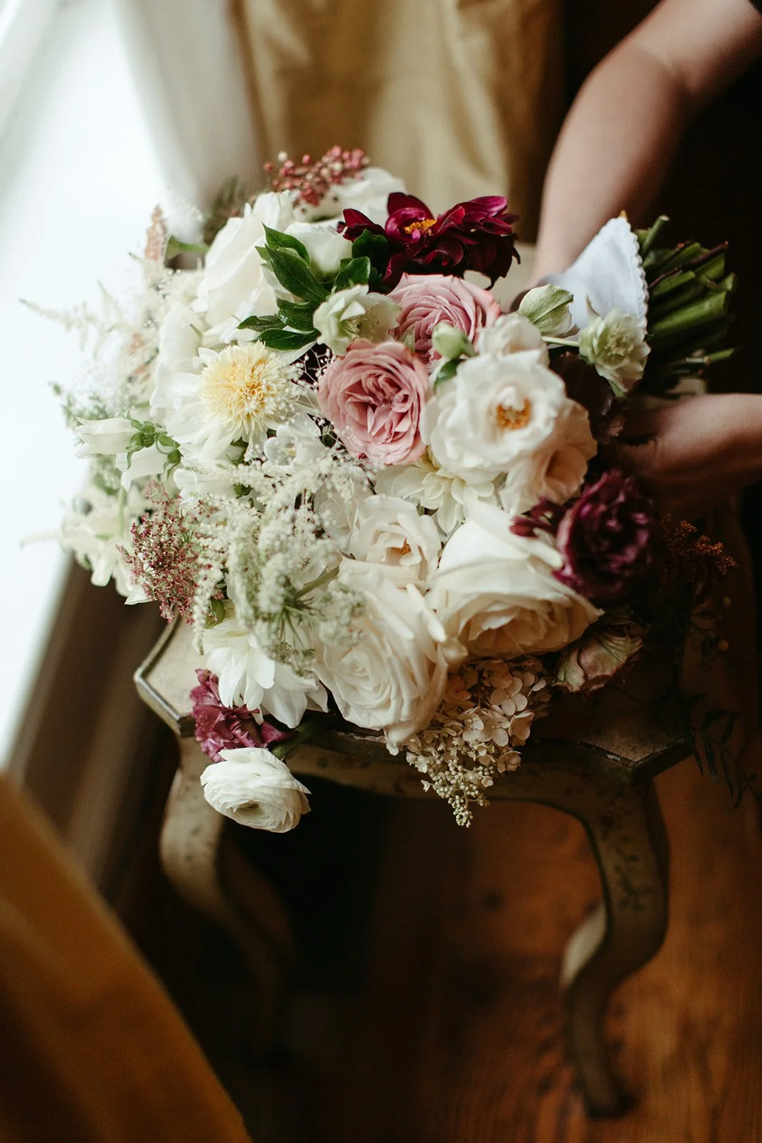 Romantic bridal bouquet with white roses, blush flowers, burgundy accents, greenery, and trailing ribbon.
