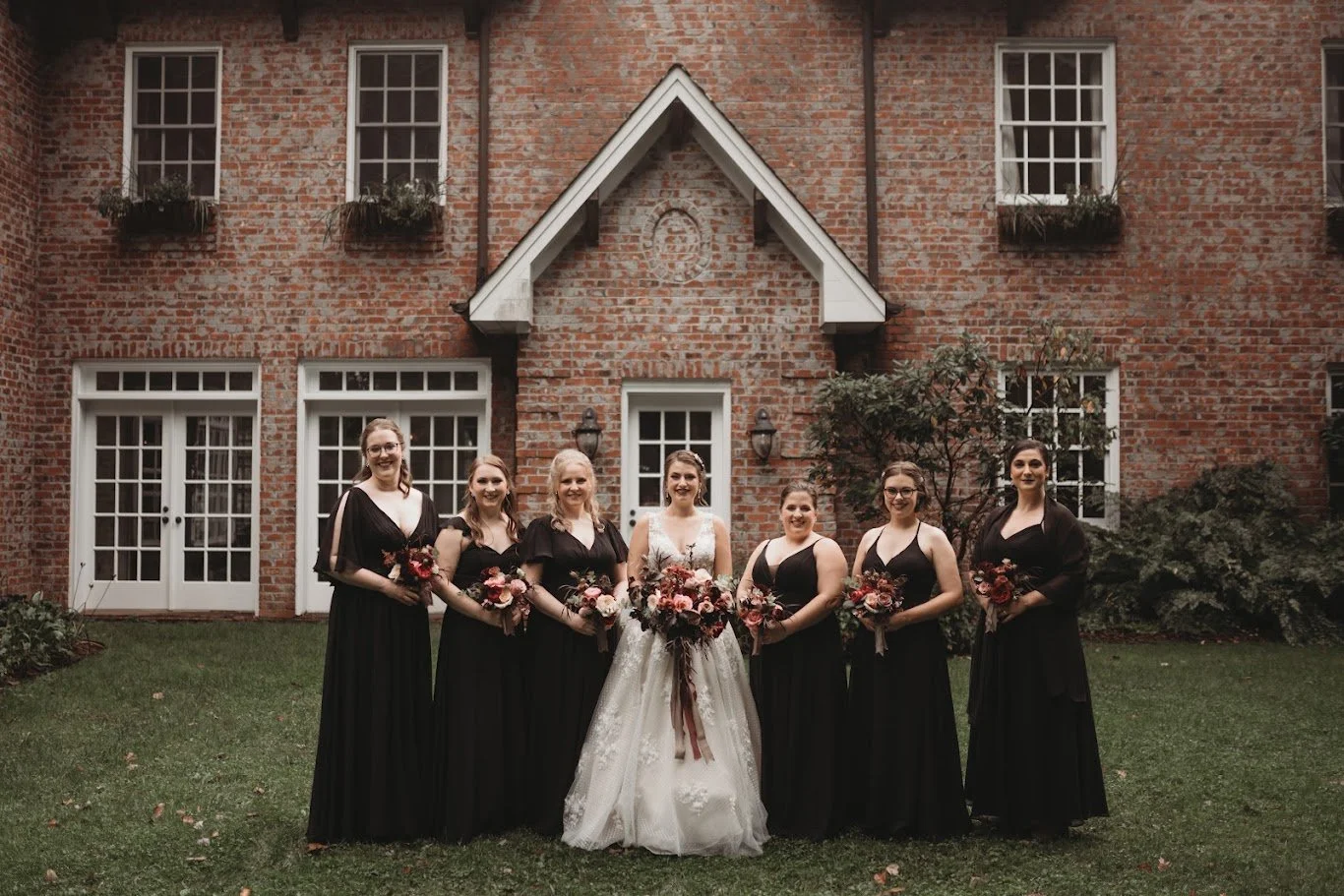 A beautiful bride in a white gown stands in the middle of her five bridesmaids, who are all dressed in black dresses.