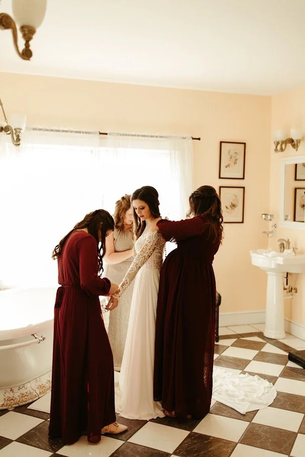 Bridesmaids helping the bride get ready in a bright room before the wedding ceremony.