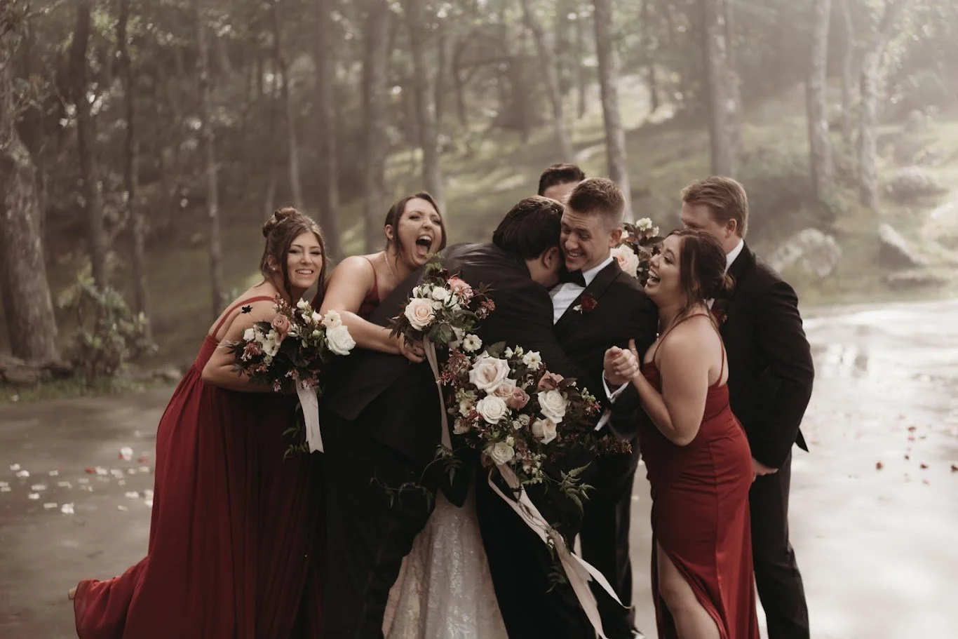 Wedding party crowding in for a group hug around the bride and groom during forest wedding portraits