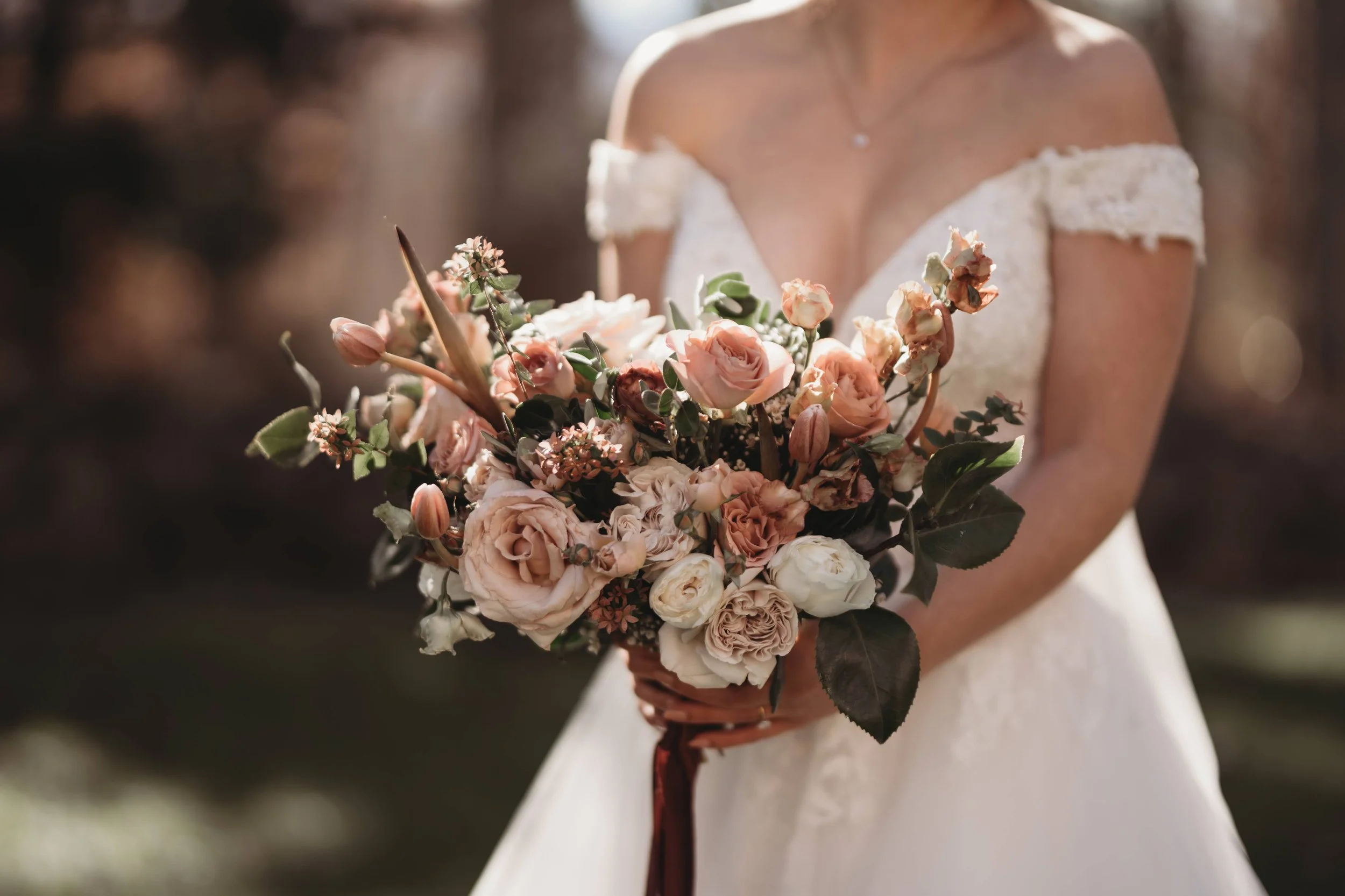 Closeup of a bridal bouquet with blush roses and burgundy accents against the wedding dress.