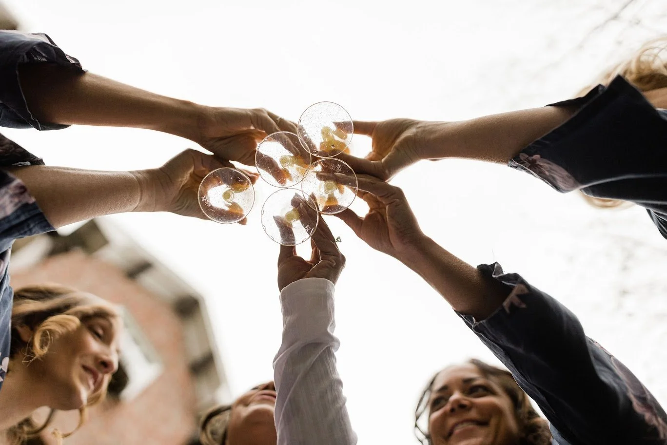 Group raises glasses for a celebratory toast outdoors, hands reaching together in the center.