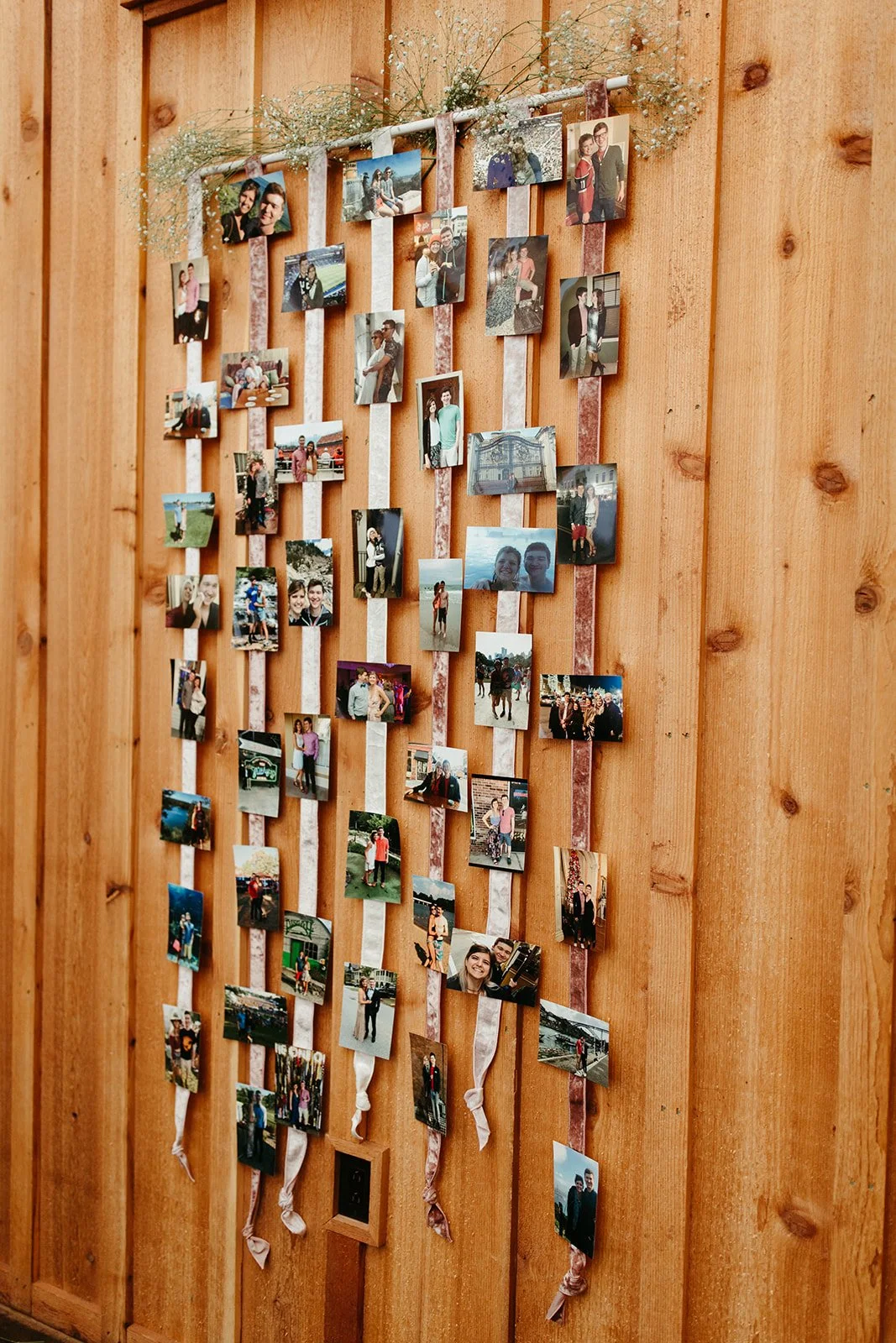 Wedding photo display with printed memories clipped to hanging ribbons on a wooden wall.