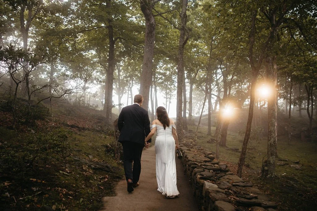 Newlywed couple walking away together on a woodland path with soft fog and warm light