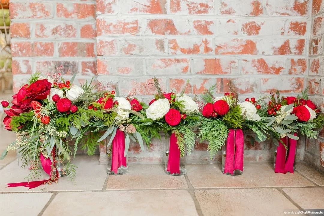 Bridesmaid bouquets with red and white roses lined up against a brick wall.