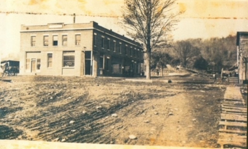 Sepia-toned historic photo of the hotel building with an unpaved road and open land beside it.