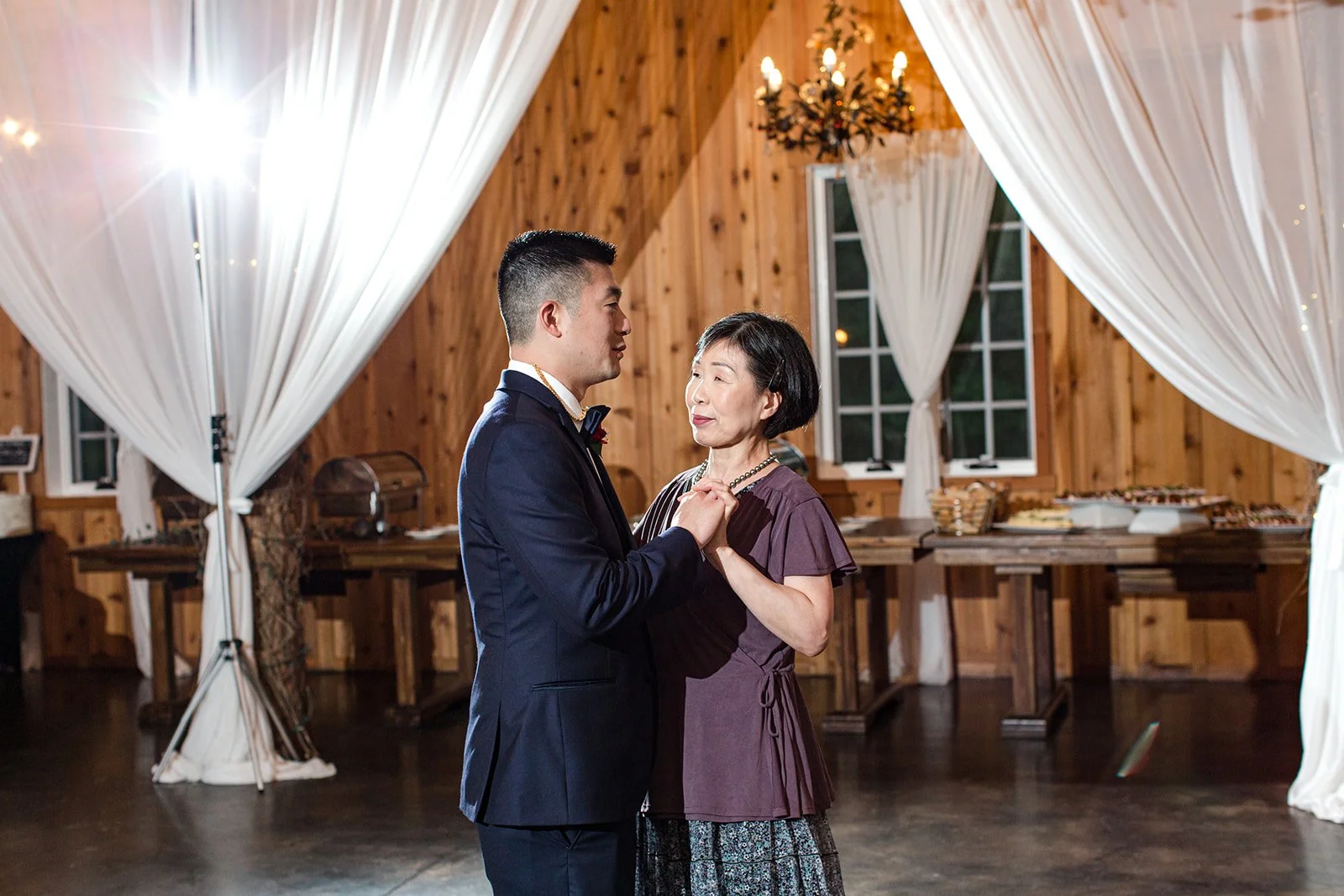 Groom dancing with his mother during a wedding reception inside a rustic wood venue.