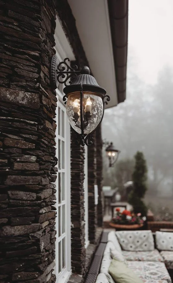Outdoor wall lantern on a stacked stone exterior with a foggy mountain patio in the background.