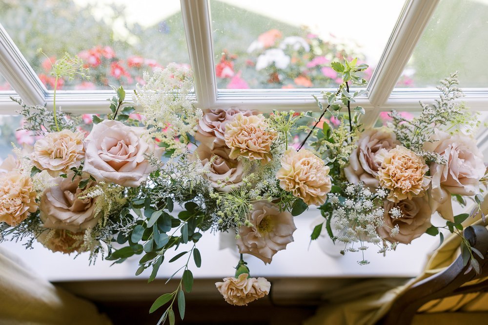Blush and peach rose floral garland with greenery arranged along a bright window ledge
