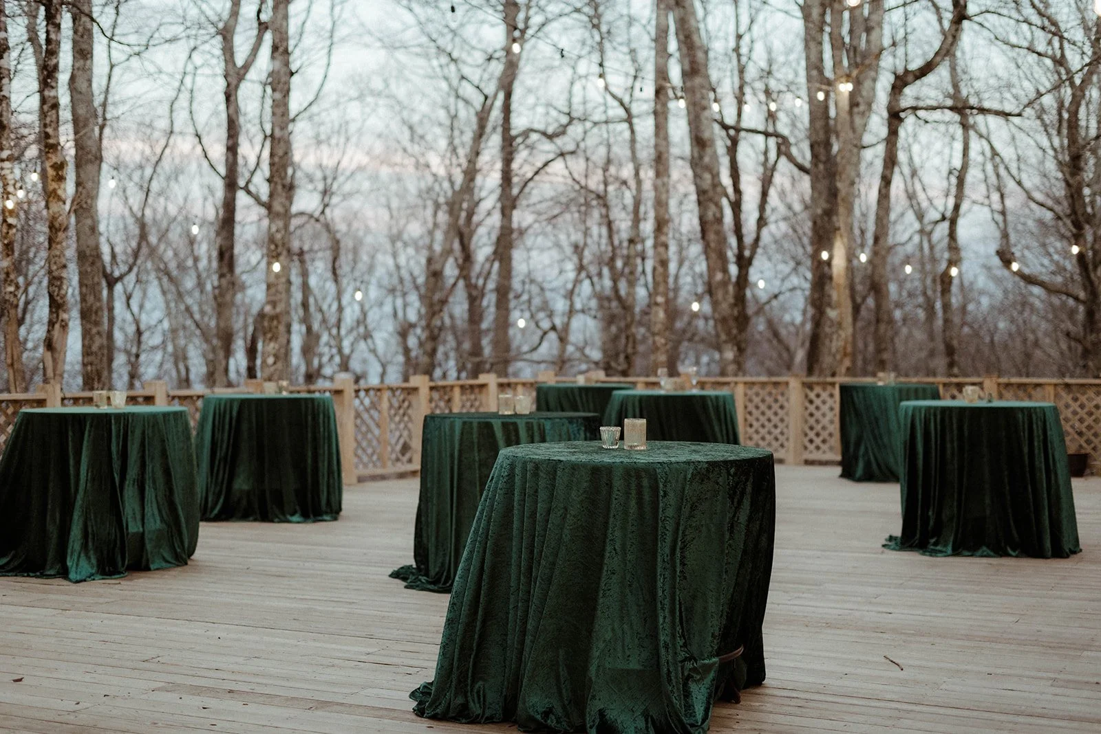 Outdoor cocktail hour setup with high-top tables covered in dark green linens on a wooden deck