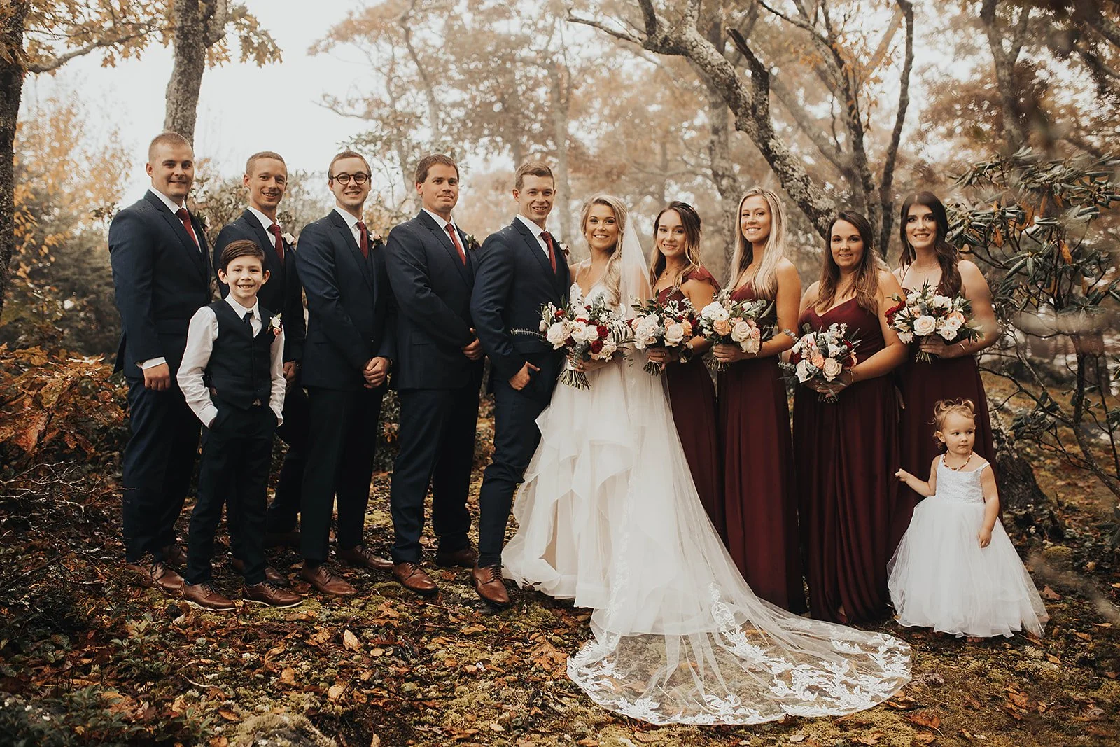 Wedding party and family formal portrait outdoors in fall woods with bridesmaids in burgundy dresses