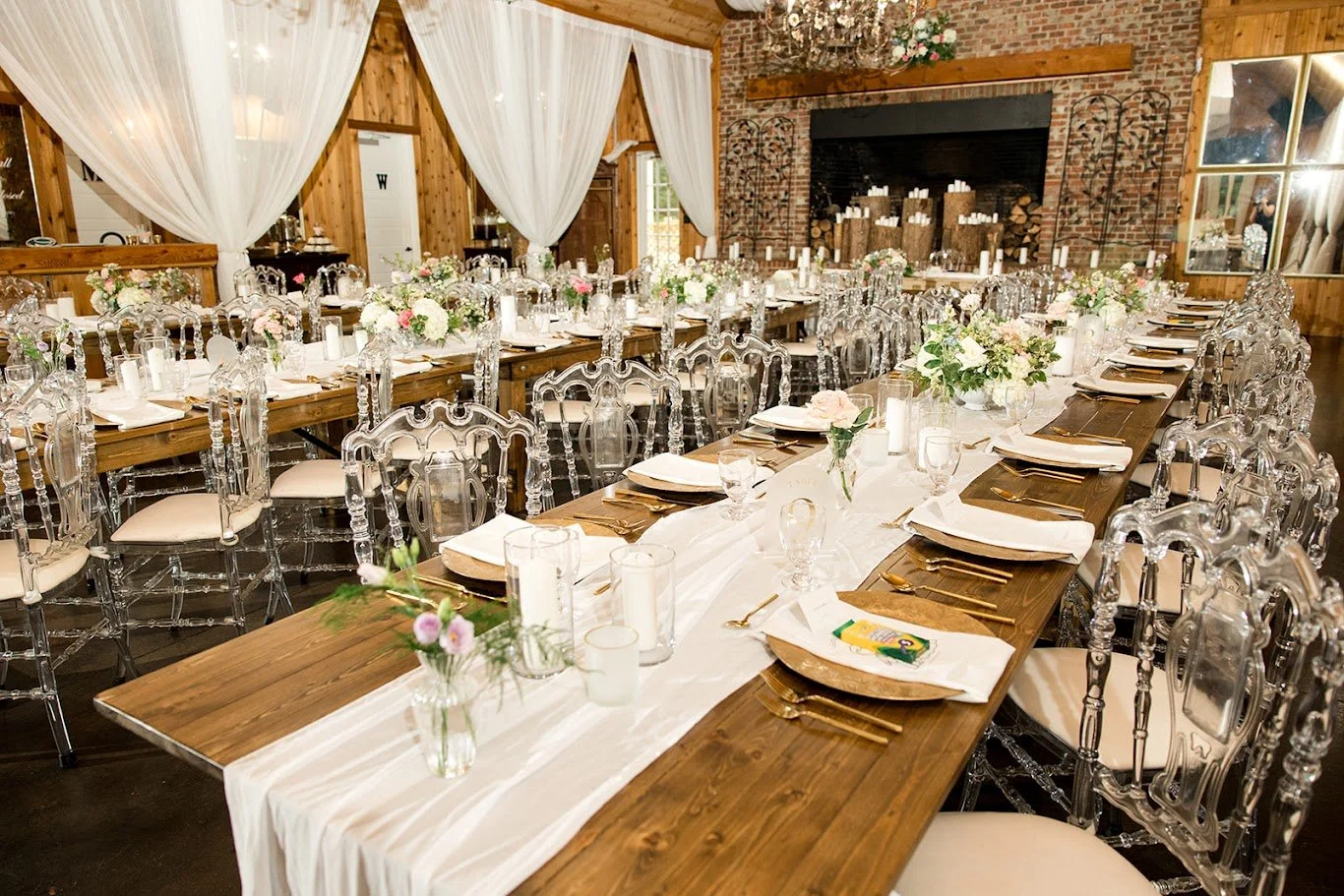 Close view of wedding reception tables with white runners, floral centerpieces, and clear chairs