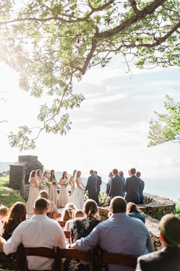 Outdoor wedding ceremony with guests seated under a tree overlooking mountain viewsOutdoor wedding ceremony with guests seated under a tree overlooking mountain views