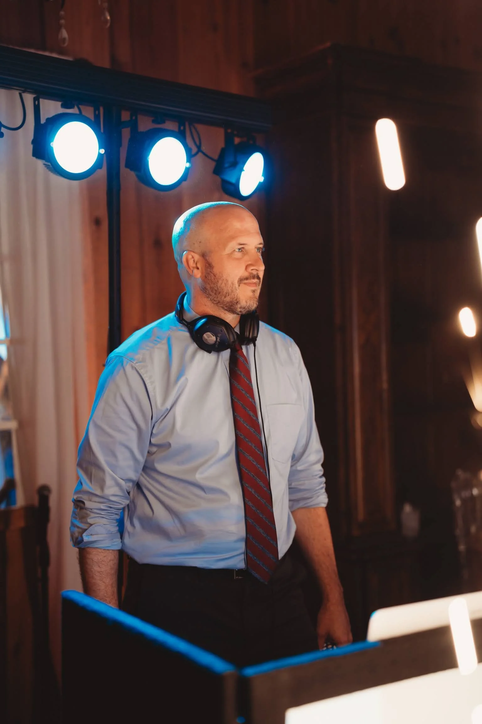 Wedding DJ standing near reception lighting and equipment inside a rustic venue