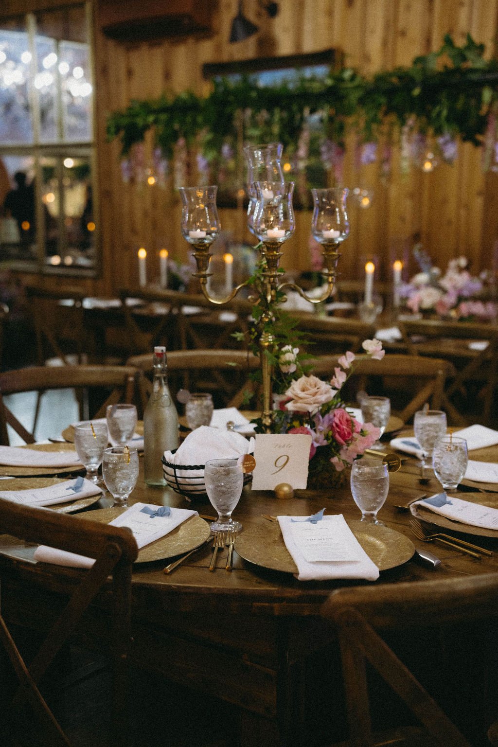 Romantic wedding reception table with gold candelabra, pastel flowers, blue napkins, glassware, and table number nine.