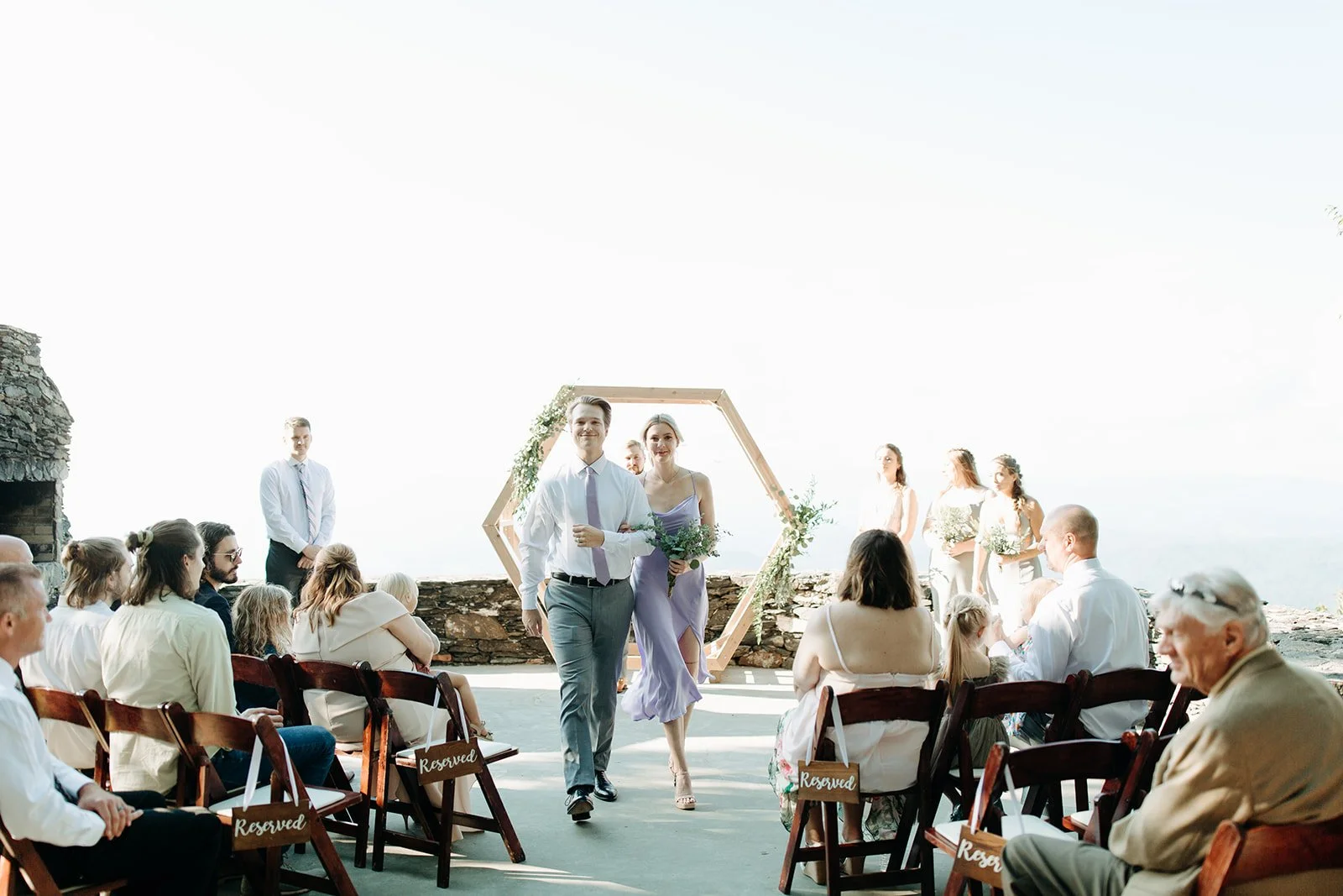 Wedding party walking down the aisle during a bright mountain overlook ceremony with reserved guest seating.