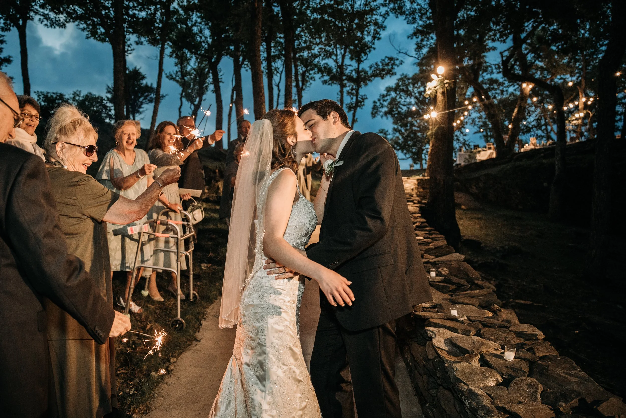 Bride and groom kissing during a sparkler exit at an evening mountain wedding celebration.