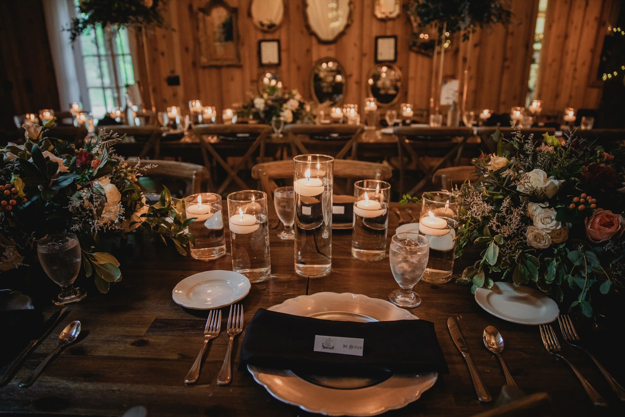 Rustic wedding reception table with candlelight, greenery garland, and place settings in a wood-paneled venue