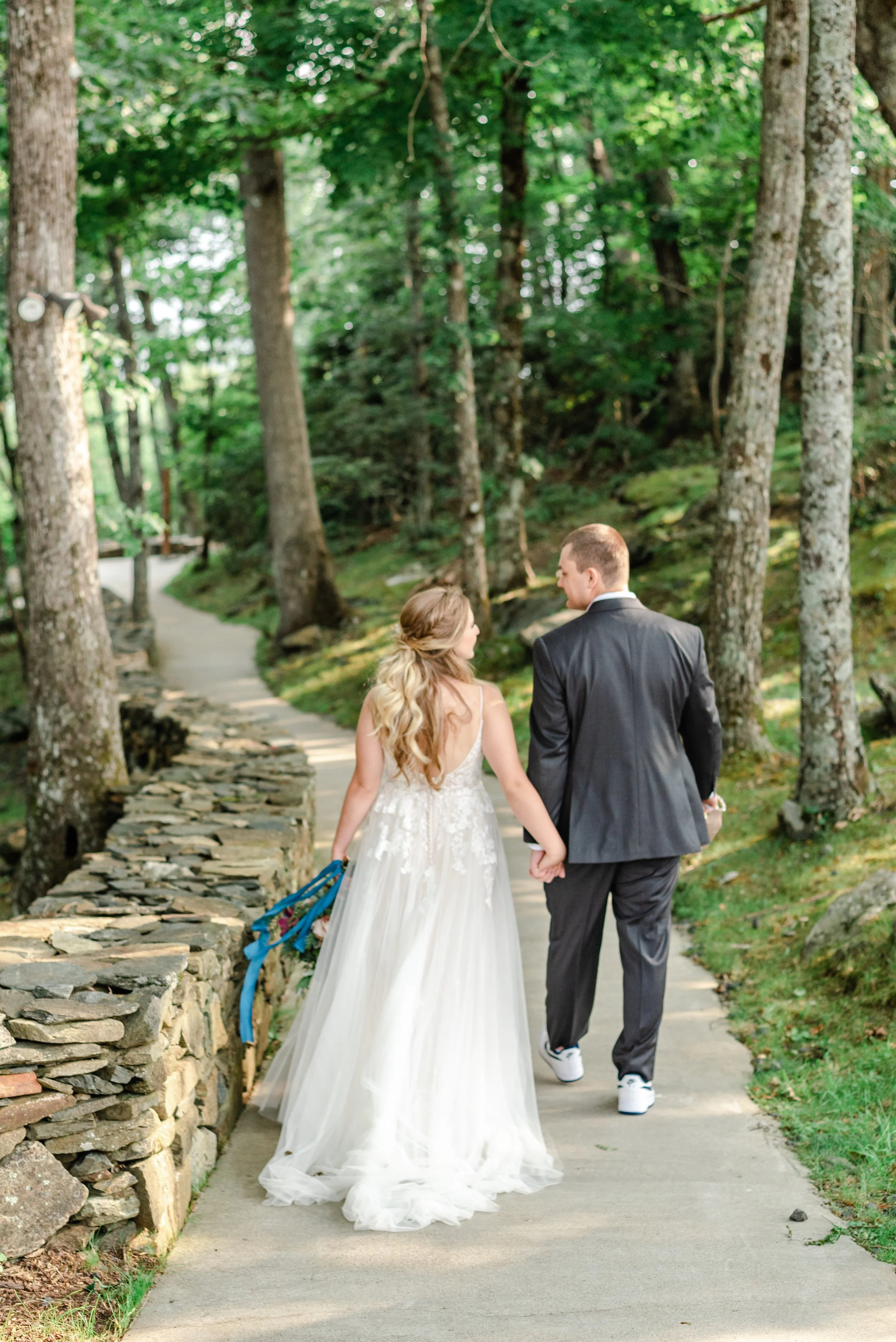 Bride and groom walking hand in hand along a forest path on their wedding day.