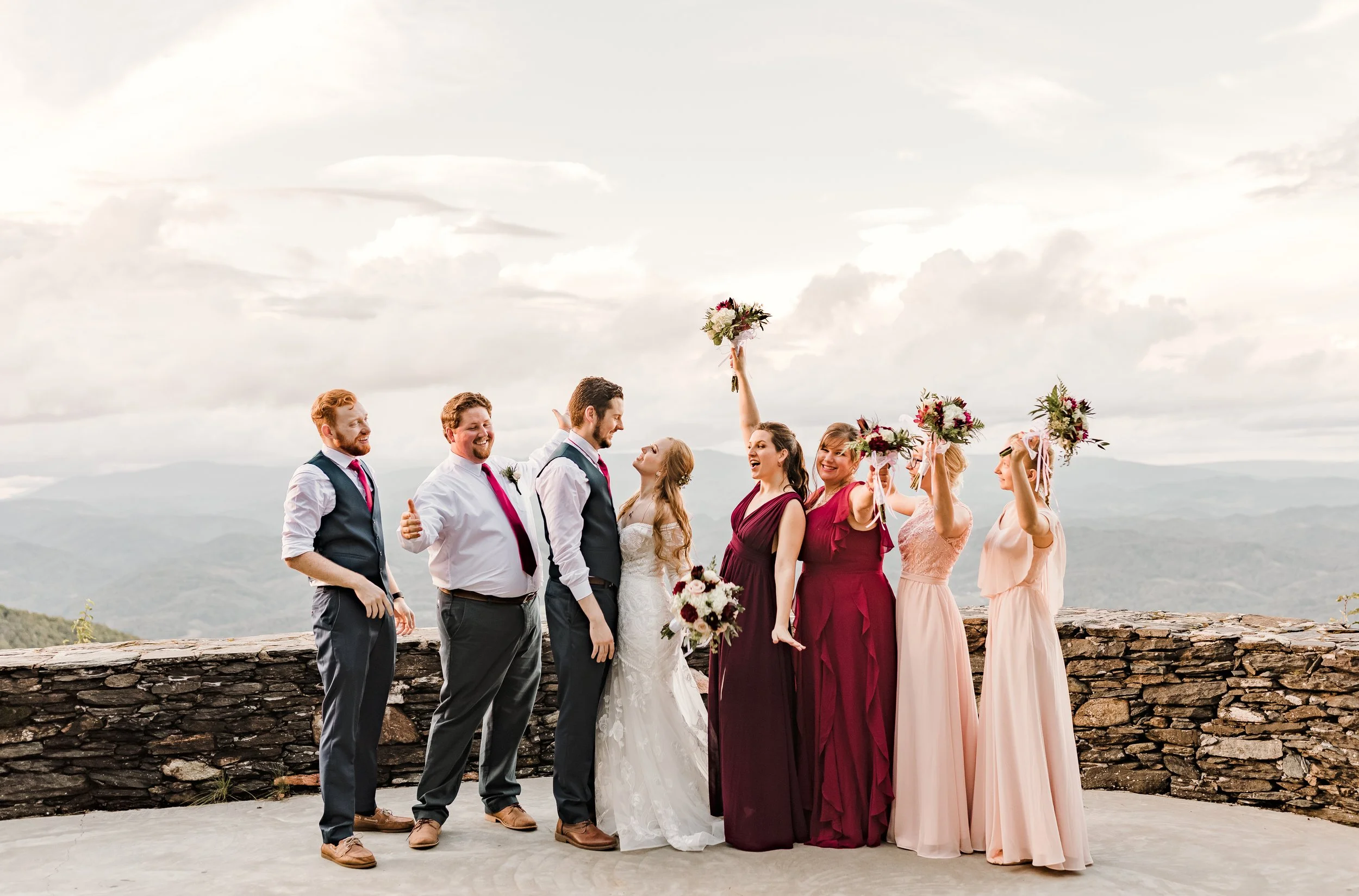 A joyous wedding party: the bride and groom gaze at each other, flanked by two groomsmen and four bridesmaids, some raising bouquets.